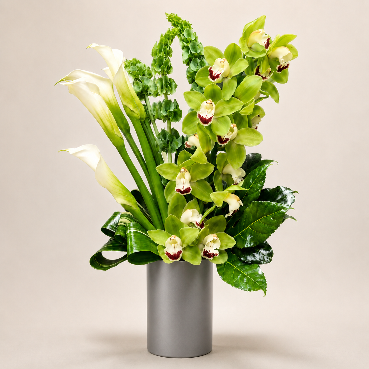 Floral arrangement with green orchids and white calla lilies in a gray vase on a beige background