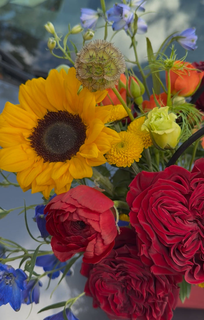 Bouquet of sunflowers, red roses, and other flowers with a blurred background