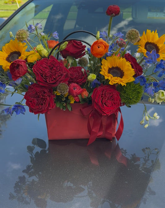 Premium designer seasonal floral tote with garden roses, sunflowers, and ranunculus in a red box arrangement.