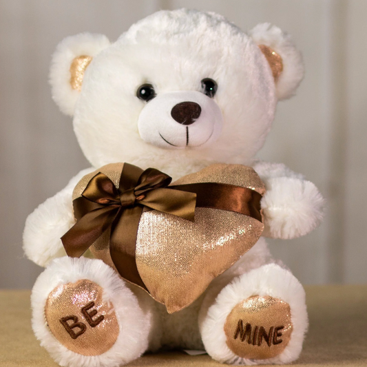 White teddy bear holding a gold gift bag with 'Be Mine' text