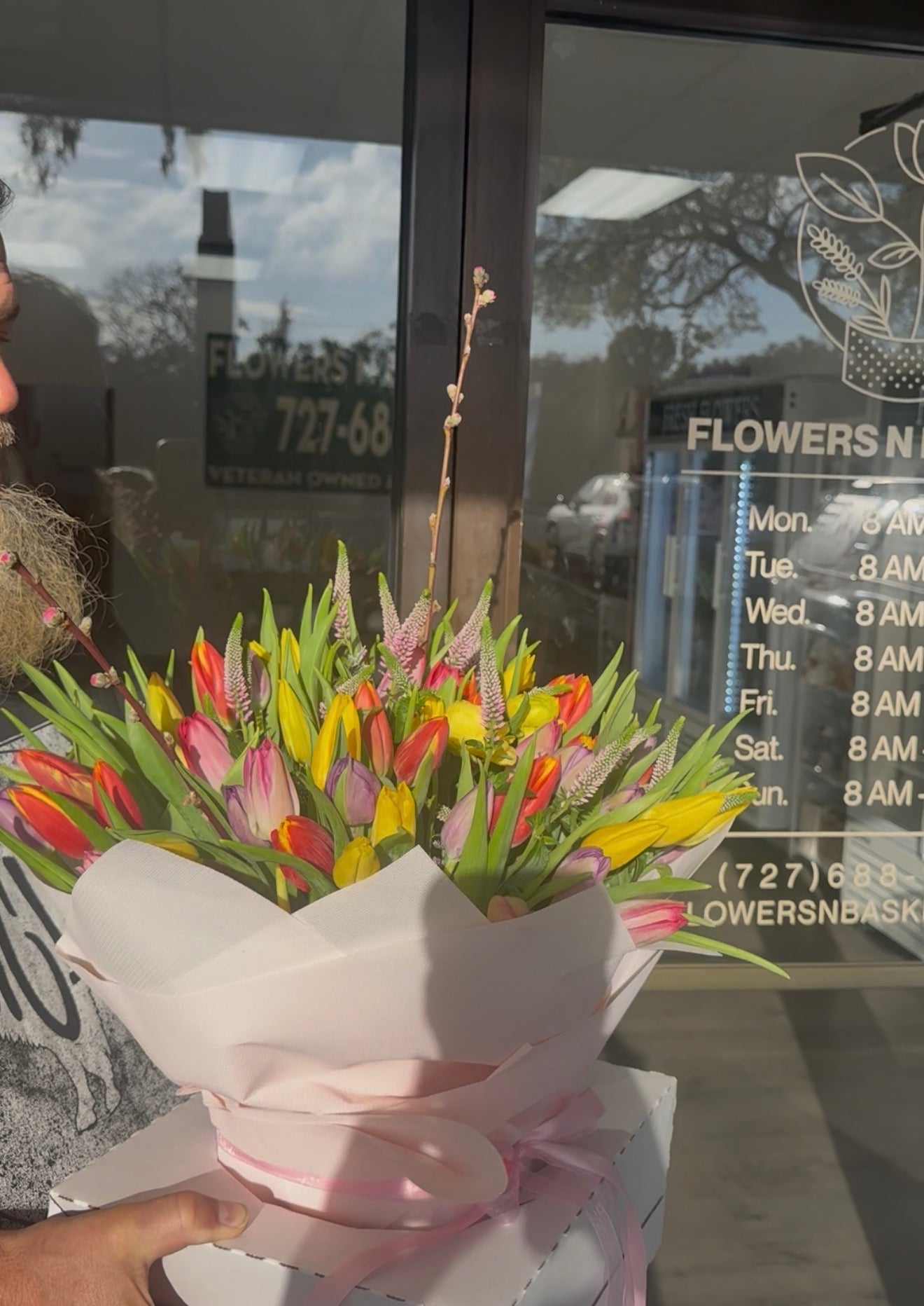 Bouquet of tulips held in front of a flower shop window.