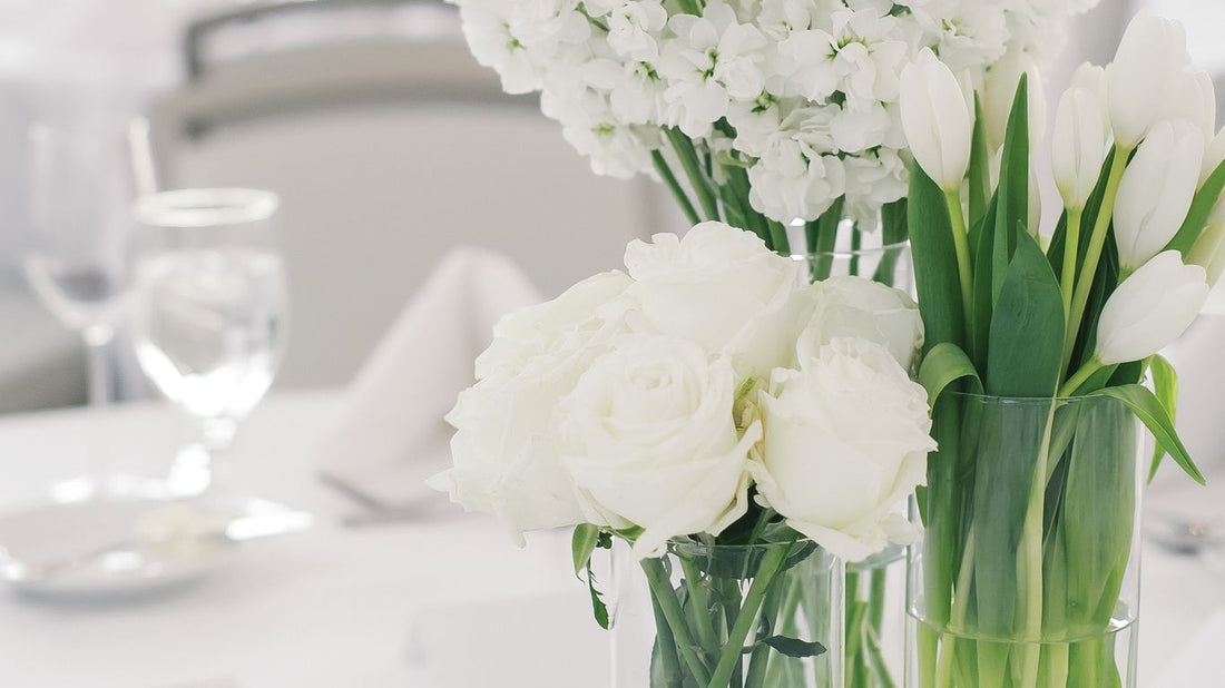 White flowers in glass vases on a mirrored surface at a formal event.