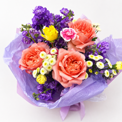Bouquet of colorful flowers wrapped in purple paper on a white background