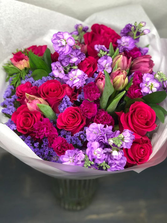 Bouquet of hot pink and purple flowers in a white paper wrap.