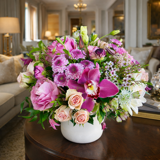 Bouquet of pink and purple flowers in a vase on a table in a living room.