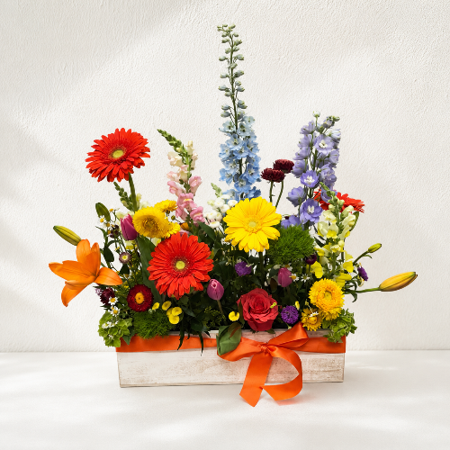Colorful flower arrangement in a box with an orange ribbon on a white background