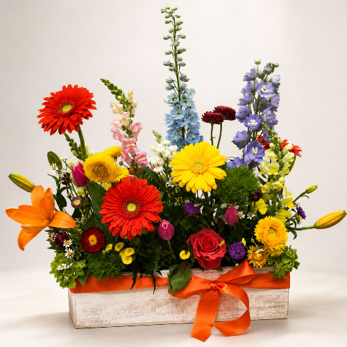 Colorful flower arrangement in a wooden box with an orange ribbon on a light background