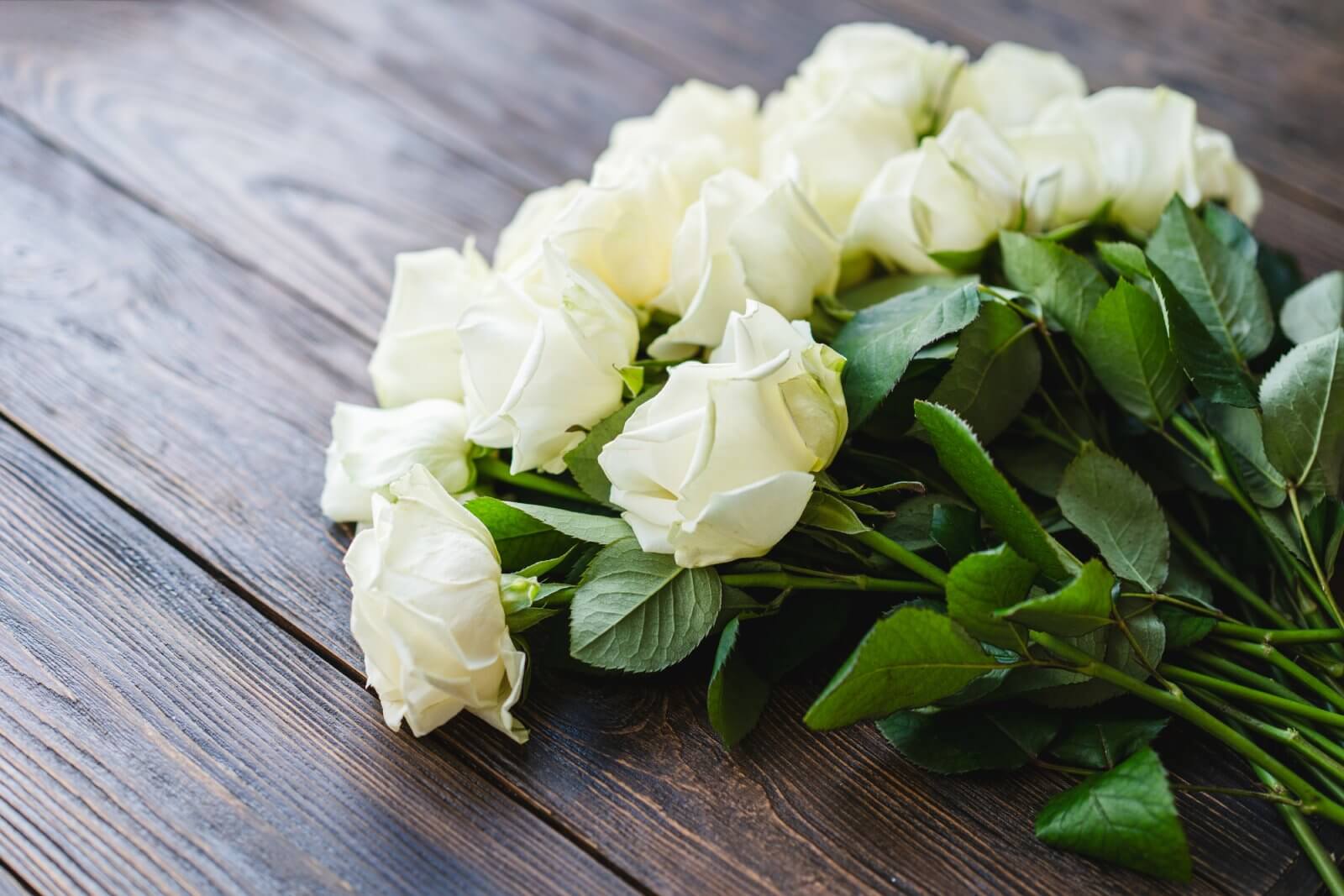 Bouquet of white roses with green leaves on a wooden surface