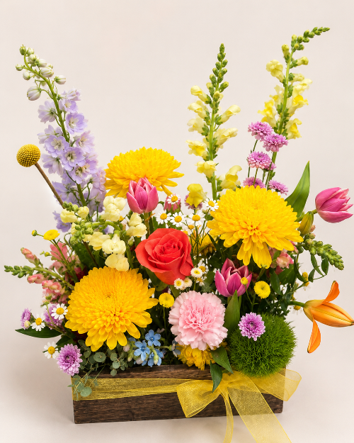 Colorful flower arrangement with yellow, pink, and red flowers in a wooden box on a light background