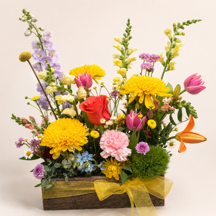 Colorful flower arrangement in a wooden box with a yellow ribbon on a light background