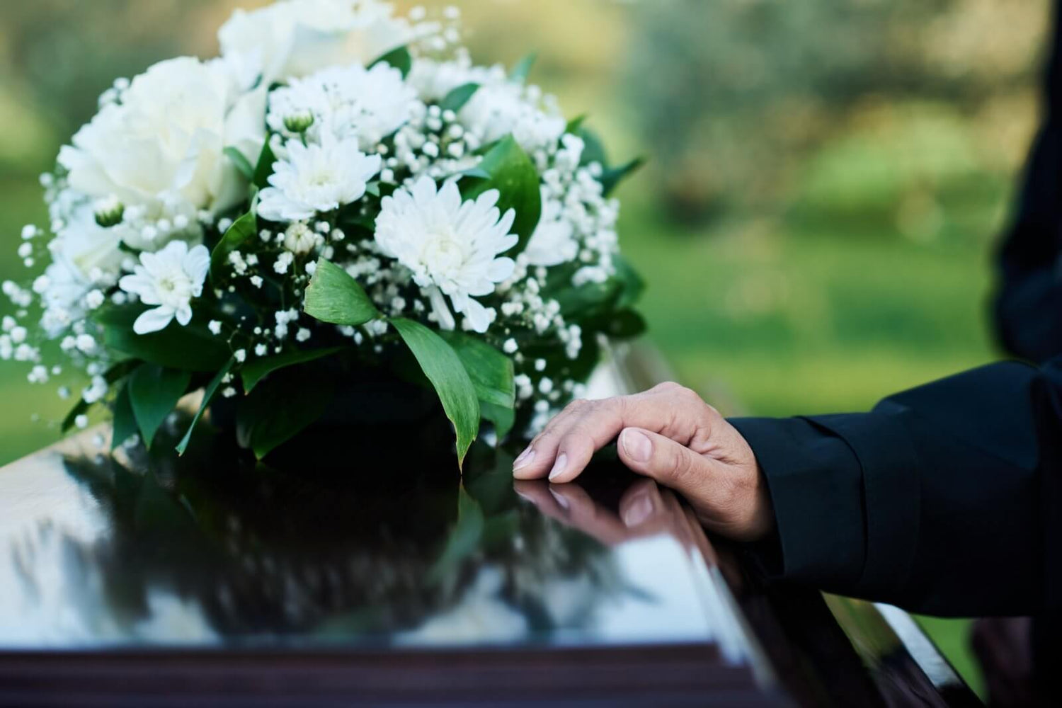 Hand touching a casket with a bouquet of white flowers in the foreground