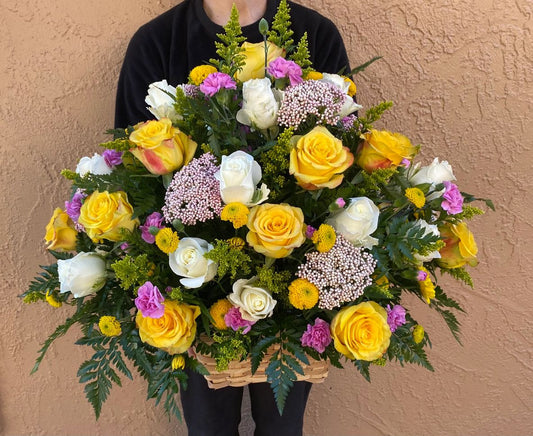 Person holding a large bouquet of colorful flowers against a beige wall.