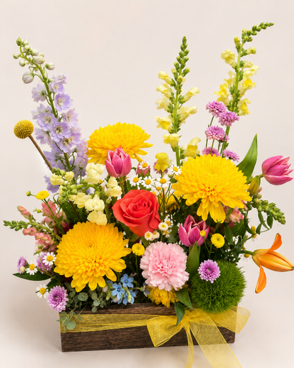 Colorful flower arrangement with yellow, pink, and red flowers in a wooden box on a light background